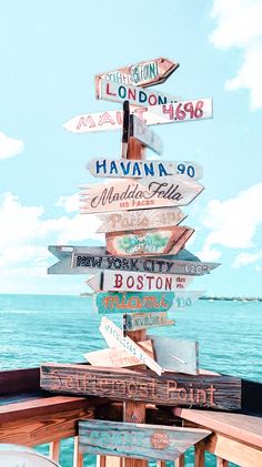 a wooden sign post with many different signs on it's side near the ocean