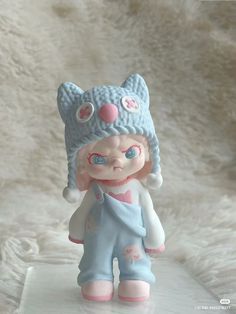 a small toy doll is wearing a hat and blue pants on a white fur background