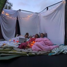 three girls in pink sleeping bags on a bed with lights strung over the top of them