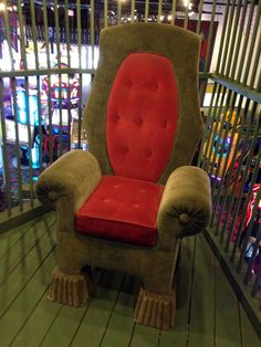 a red chair sitting on top of a wooden floor next to a metal fence with lights in the background