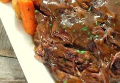 a white plate topped with meat and gravy next to carrots