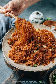 someone holding chopsticks over noodles in a bowl