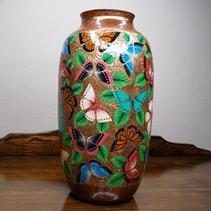 a vase with butterflies painted on it sitting on a wooden table next to a wall