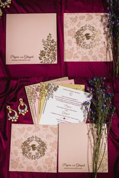 the wedding stationery is laid out on top of the red satin with purple flowers