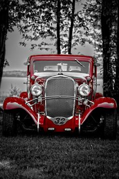 an old red car is parked in the grass