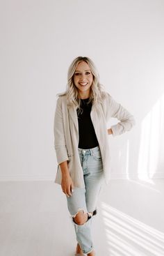 a woman standing in front of a white wall wearing ripped jeans and a blazer