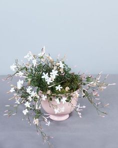 small white flowers in a pink vase on a gray tablecloth with grey wall behind it