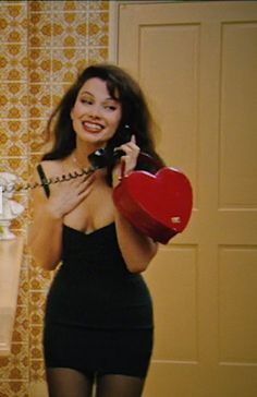 a woman is talking on the phone and holding a heart shaped object in her hand