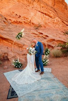 a bride and groom standing in front of a rock formation at their desert wedding ceremony