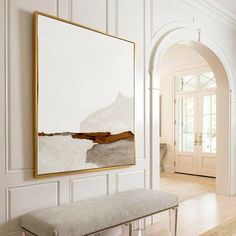 a large painting hangs on the wall above a bench in front of a white door