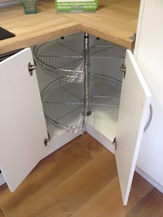 an open cabinet in the corner of a kitchen with wood flooring and white cabinets