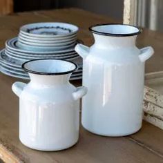 two white vases sitting on top of a wooden table next to plates and bowls