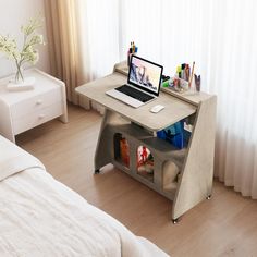 a laptop computer sitting on top of a wooden desk next to a bed with white sheets