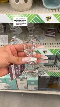 a person is holding a small glass object in their hand at a store shelf with other items on the shelves behind them