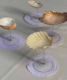 three seashells are placed on glass holders with silverware in the shape of wine glasses