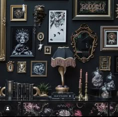 a black wall with many framed pictures and other items on it, including a lamp