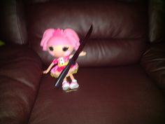 a little doll sitting on top of a brown couch holding a large pair of scissors