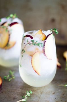 two glasses filled with ice and fruit on top of a table next to sliced apples