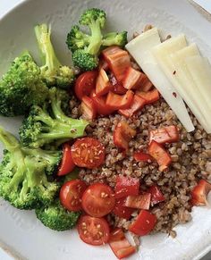 a white plate topped with rice, broccoli and sliced up red tomatoes next to cheese