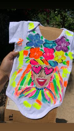 a person holding up a shirt that has been painted with colorful flowers and a woman's face on it