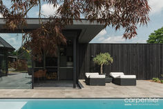 an outdoor living area next to a pool with chairs and a tree in the foreground