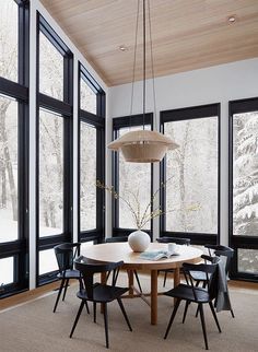 a dining room table with chairs and a vase on the table in front of large windows