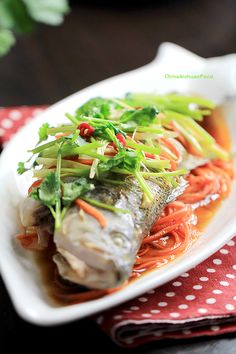 a white plate topped with fish and veggies on top of a red napkin