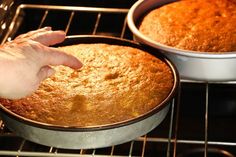 a person touching the bottom of a cake in an oven with two pans on it