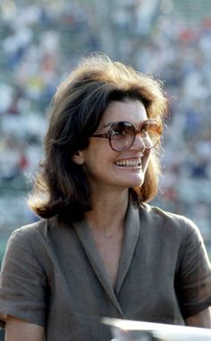 a woman wearing glasses and smiling at the camera in front of a large group of people