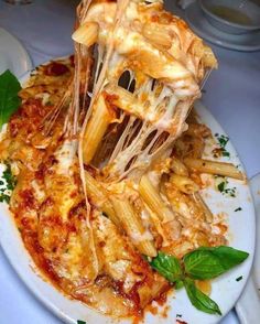 a white plate topped with lasagna and cheese covered in melted sauce, garnished with basil leaves