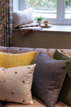 the pillows are lined up on the couch in front of the window, and there is a potted plant next to it