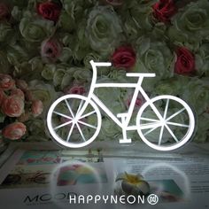 a lighted bicycle is sitting on top of a table next to flowers and an open book