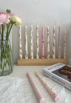 several candles are lined up on a table next to a book and vase with flowers