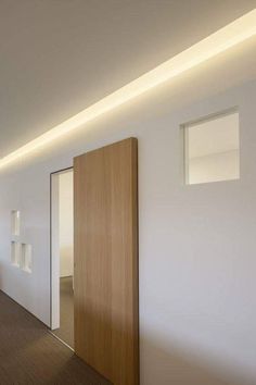 an empty hallway with white walls and wooden door, lights on the ceiling and wood flooring