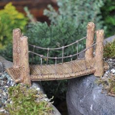 a miniature bridge made out of wood and rope sitting on some rocks with moss growing around it