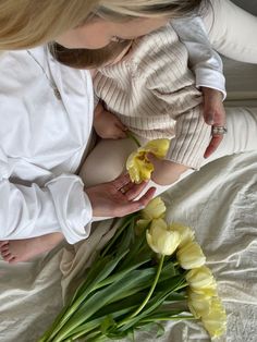 a woman holding a baby on her lap with yellow flowers in front of her face