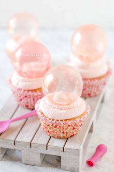 three cupcakes with pink frosting and snowballs on top, sitting on a wooden table