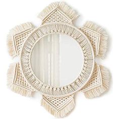 a round mirror with tassels around the edges on a white wall mounted shelf