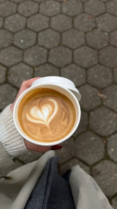 a person holding a cup of coffee with a heart drawn on it's foam