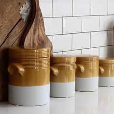 three yellow and white ceramic canisters with wooden spoon on the side next to each other