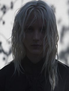 a man with blonde hair standing in front of a tree