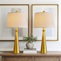 two lamps sitting on top of a wooden table next to a vase with a plant in it