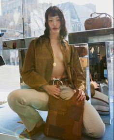 a woman is sitting on the ground holding a purse and posing for a photo in front of a store window