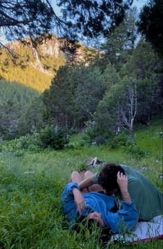 two people are laying in the grass with their backs to each other and one person is covering his face