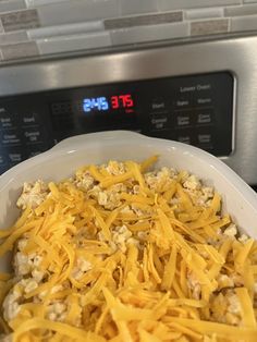 a casserole dish with cheese on top in front of an oven and clock