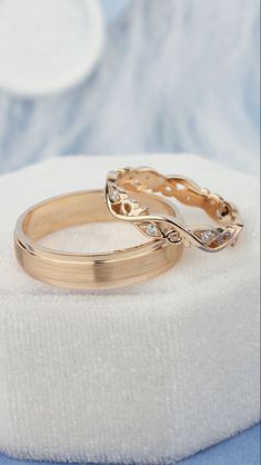 two gold wedding rings sitting on top of a white ring pillow in front of a blue and white background