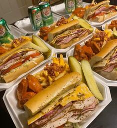 several trays filled with sandwiches and pickles next to cans of soda on a table