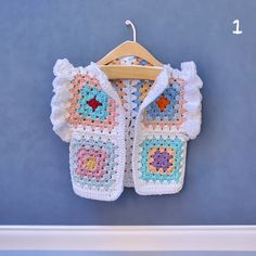 a crocheted jacket hanging on a wall with a wooden hanger next to it