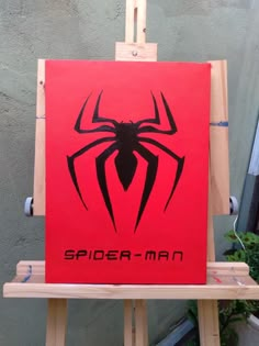 a red spiderman sign sitting on top of a wooden easel