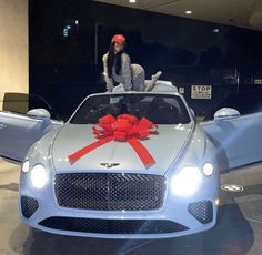 a woman standing on top of a white car with a red bow tied around it